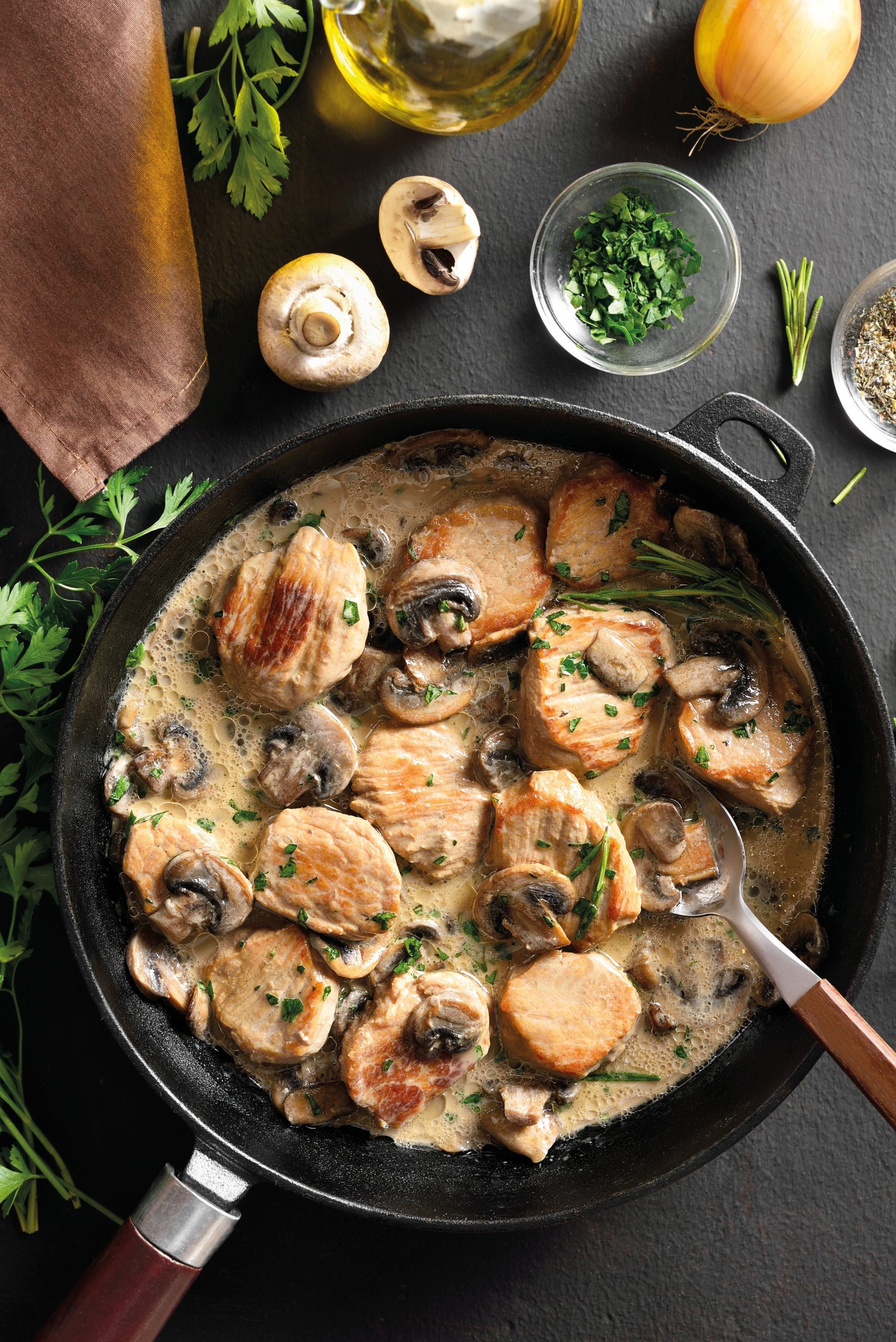Pork medallions in mushroom gravy in cast iron pan over dark stone background. Top view, flat lay