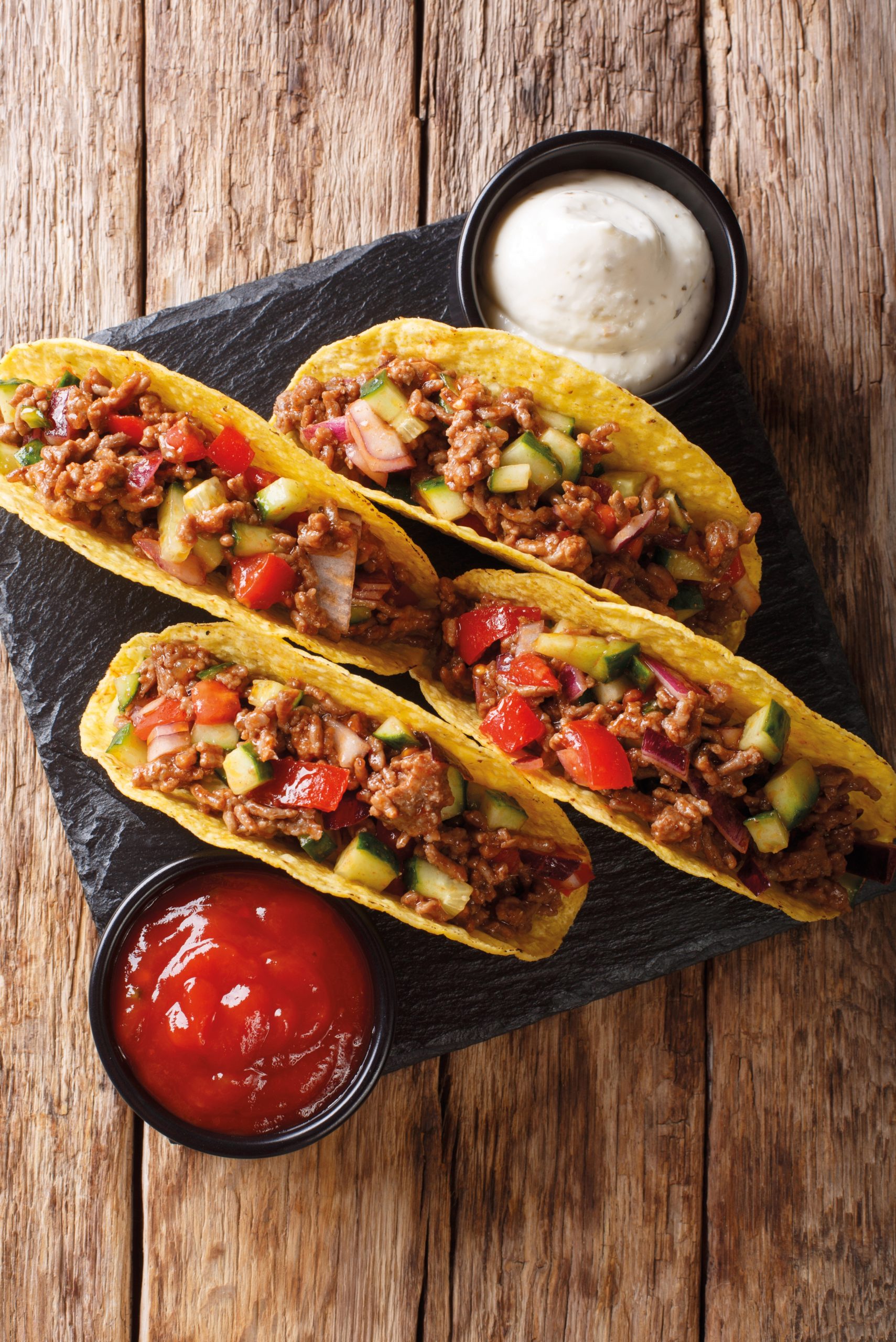 Mexican tacos stuffed with minced beef and vegetables close-up on the table. Vertical top view from above